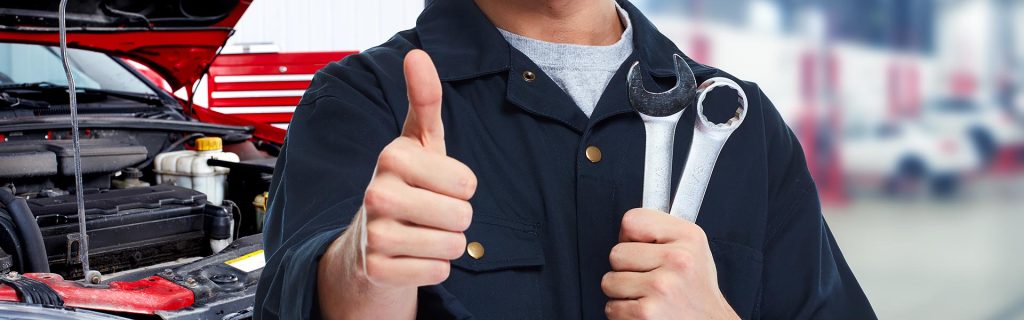 Certified Buick Maintenance Professional holding silver tools gives a thumbs up as he is working on the engine of a red S*UV