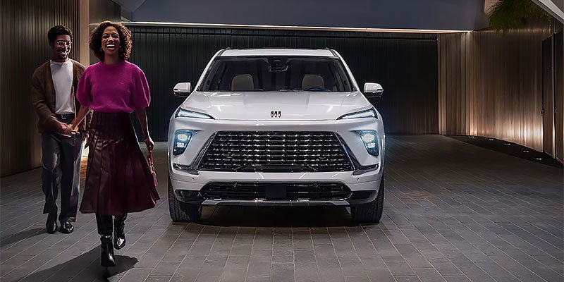 An excited couple stand beside a white 2026 Buick Enclave
