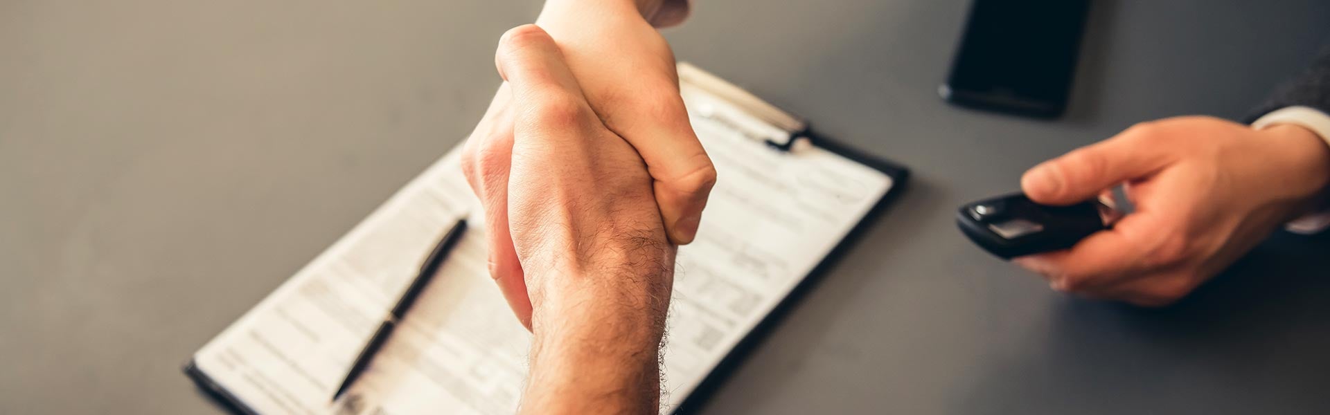 A customer and a salesperson's handshake over the paper agreement for purchasing a vehicle and keys being given to the purchaser.